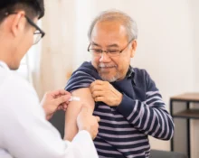 A smiling elderly man receives a shingles vaccine shot from a healthcare professional, symbolising the importance of immunisation against shingles and its complications.