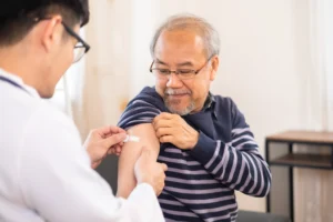 A smiling elderly man receives a shingles vaccine shot from a healthcare professional, symbolising the importance of immunisation against shingles and its complications.