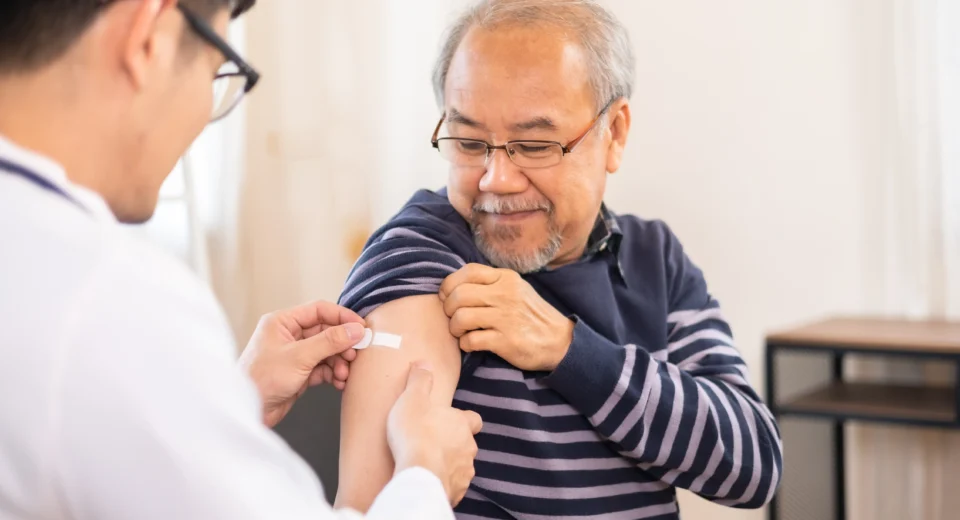 A smiling elderly man receives a shingles vaccine shot from a healthcare professional, symbolising the importance of immunisation against shingles and its complications.