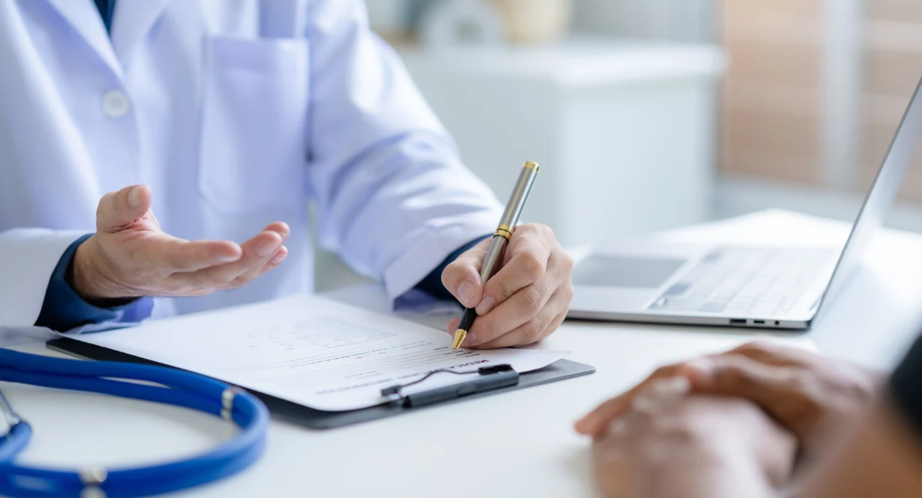 A doctor consulting a patient, taking notes on a medical document, symbolizing expert haematology consultation in Singapore and Malaysia for second opinions.