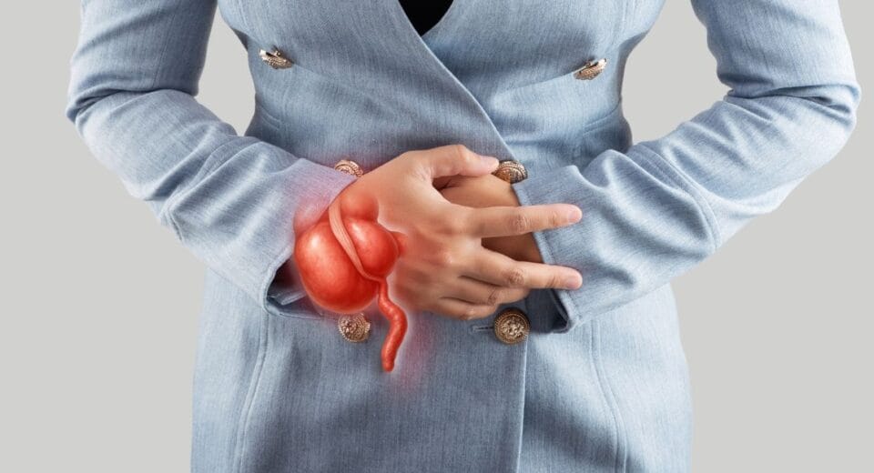 A person in a blue blazer clutches their abdomen, showing discomfort. An overlay of a highlighted red stomach suggests stomach pain or digestive issues.
